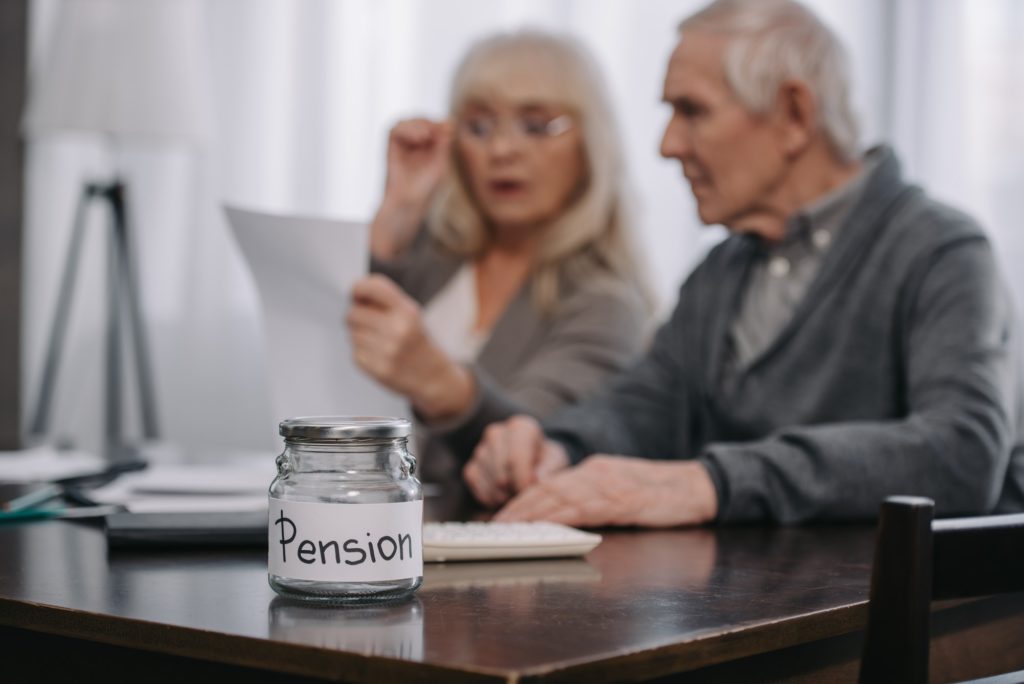 selective focus of glass jar with 'pension' word on table and senior couple on background