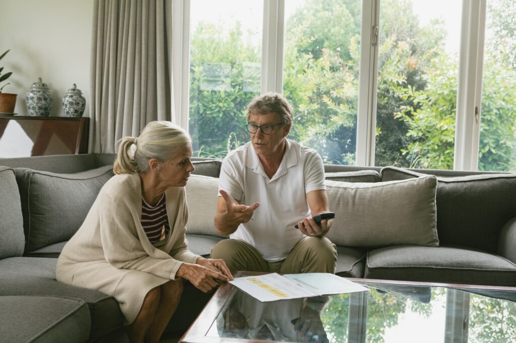 Active senior Caucasian couple calculating domestic bills on sofa in living room at comfortable home